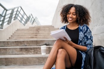 Portrait of young afro-american woman writing in a notebook while sitting outdoors on stairs.