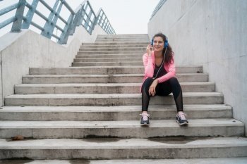 Portrait of an athletic woman listening to music on a break from training while sitting on stairs. Sport and health lifestyle concept.