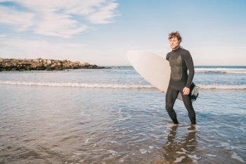 Portrait of young surfer leaving the water with surfboard under his arm. Sport and water sport concept.