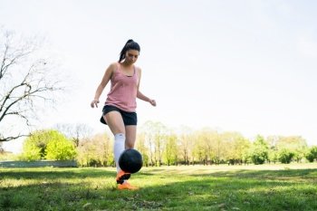 Portrait of young female soccer player running around cones while practicing with ball on field. Sports concept.