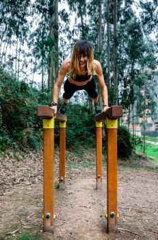 Happy athlete woman training on parallel bars in a park. Athlete woman training on parallel bars