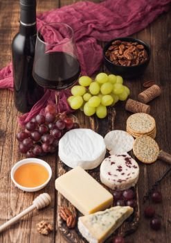 Glass and bottle of red wine with selection of various cheese on the board and grapes on wooden table background. Blue Stilton, Red Leicester and Brie Cheese and knife with honey.