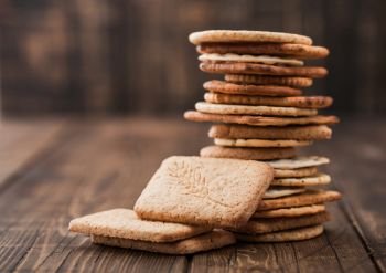 Stack of various organic crispy wheat, rye and corn flatbread crackers with sesame and salt on wood background.