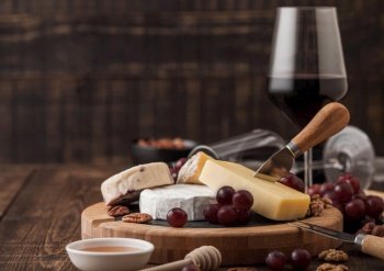 Glass of red wine with selection of various cheese on the board and grapes on wooden table background. Blue Stilton, Red Leicester and Brie Cheese and knife with honey.