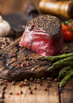 Slice of Raw Beef Topside Joint with Salt and Pepper on wooden chopping board with tomatoes garlic and asparagus tips on wood kitchen table.