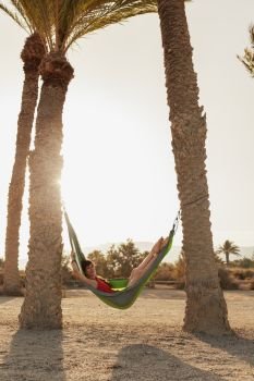 Young woman lying in his hammock among palm trees on the beach