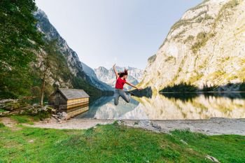 Young woman jumping on a pier near a lake under the mountains