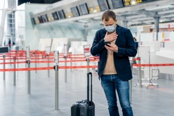 Businessman walks in airport terminal, has problems with breathing checks email box on smartphone stands near luggage wears disposable medical mask as coronavirus outbreak prevention. Health awareness