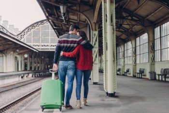 Relationship and travelling concept. Lovely woman and man cuddle while walk across railway station platform, carry suitcase, express love and support, stand closely to each other, have journey