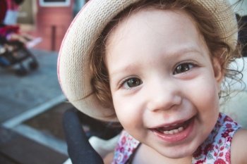 Close-up portrait of cute baby girl looking at camera smiling and wearing a hat