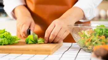 young Asian woman is preparing healthy food vegetable salad by Cutting ingredients on cutting board on light kitchen, Cooking At Home and healthy food concept.