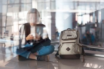 waiting for a flight at the airport. girl with a phone and a backpack sits on the floor
