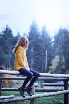 girl sitting on a wooden fence. relaxation in a mountain hut
