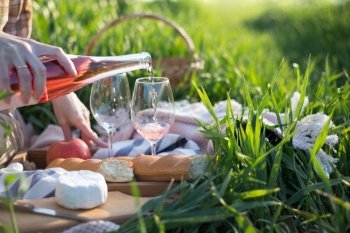 Summer - Provencal picnic in the meadow.  girl  pours wine into glasses  near a picnic basket and baguette
