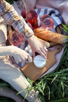 Summer - Provencal picnic in the meadow.  girl  cuts brie cheese  near a picnic basket and baguette, wine, glasses

