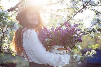 summer - beautiful girl in hat and suspenders at the garden with a bouquet of lilacs
