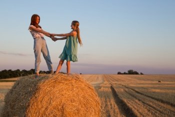 happy family in a wheat field. mother and daughter posing on a Round Bales at sunset time.
