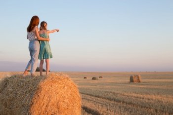 happy family in a wheat field. mother and daughter posing on a Round Bales at sunset time.
