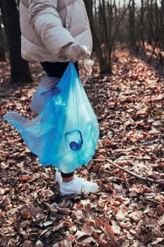 Young woman cleaning up a forest. Volunteer picking plastic waste to bags. Concept of plastic pollution and too many plastic waste. Environmental issue. Environmental damage. Responsibilitiy for environment. Real people, authentic situations
