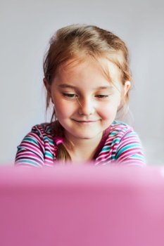 Little girl preschooler learning online solving puzzles playing educational games listetning to sounds watching video on tablet during COVID-19 quarantine sitting at desk in front of computer looking at screen