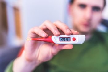 Man is holding a red fever thermometer in his hand