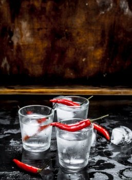 Vodka shots with chili pepper. On a wooden background.. Vodka shots with chili pepper.