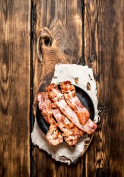 Fried bacon in a frying pan. On a wooden table.. Fried bacon in a frying pan. On wooden table.