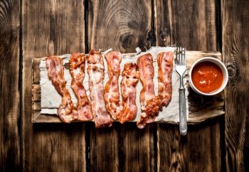 Fried bacon with tomato sauce. On a wooden background.. Fried bacon with tomato sauce. On wooden background.