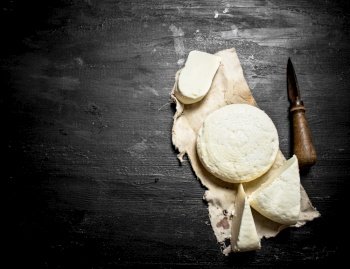 Fresh goat cheese with an old knife. On a black wooden background.. Fresh goat cheese with an old knife.