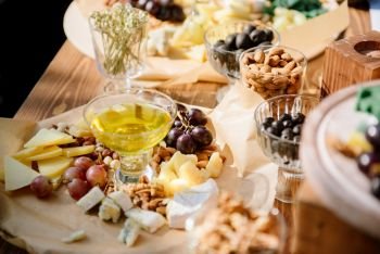Different kinds of cheese with wine, figs, walnuts, ham, grapes, honey, toast. In a rustic style.. Cheese set on a plate laid out on a beige background. Different types of cheeses: Camembert, Parmesan, blue cheese, olives