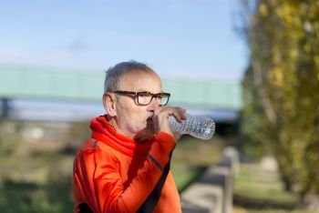 Senior runner drinking water after jogging