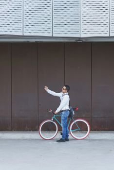 Hipster man taking a selfie . He is commuting, he has a fixed gear bike. Lifestyle, travel and sustainability concepts.