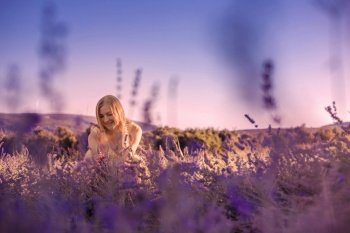 Blonde woman in a yellow dress in lavender field at sunset. Lavender bloom season. Enjoyment of unity with nature. Meditation and relaxation outdoor