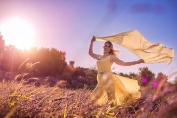 Blonde woman in a yellow dress in lavender field at sunset. Lavender bloom season. Enjoyment of unity with nature. Meditation and relaxation outdoor