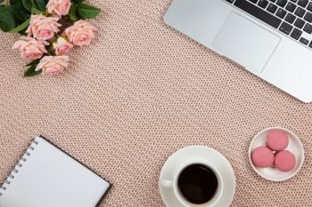 Work from home concept. Modern female working space, top view. Laptop, coffee, cakes, roses, notebook on knitted blanket, copy space, flat lay. Desktop of freelancer. Frame of objects. Horizontal.