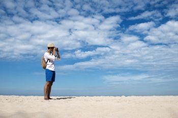 Young man travel outdoor on tropical beach with blue sky and white cloud using DSLR professional camera take a photo on vacation time with love nature. Outdoor travel lifestyle concept.