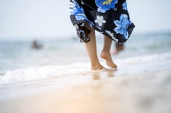Woman bare foot walking on summer beach. close up leg of young woman walking along wave of sea water and sand on vacation beach. Enjoyment barefoot walk outdoor with freedom. Relaxation Travel Concept.