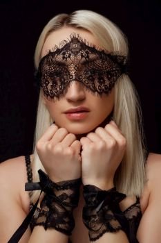 portrait of a young beautiful blonde woman in a lace face mask and lace handcuffs on a black isolated background