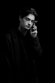  young guy in a black hoodie on a black background with a mobile phone in his hands