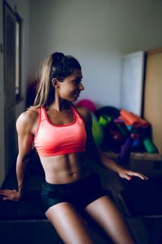 Midsection of young muscular fit fitness woman sporty sportswoman sitting on the bench at the gym posing her muscles body