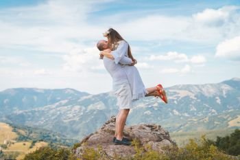 Young couple wearing white on the top of the mountain rock man holding his girl friend wife fiancee up hugging and kissing couple in love