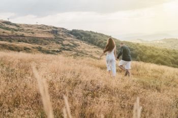 Young couple man and woman in love walking on the field on the mountain in autumn or summer day hugging together having fun bonding flirting flirt husband and wife lovers