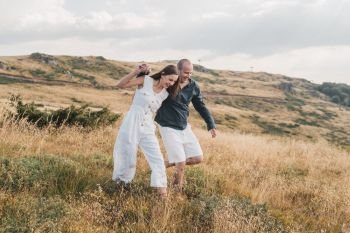 Young couple man and woman in love walking on the field on the mountain in autumn or summer day hugging together having fun bonding flirting flirt husband and wife lovers