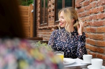 Portrait of beautiful caucasian woman blonde girl sitting by the table at cafe in summer or spring day looking to the side smiling wear dress daily routine with positive emotion and joy concept