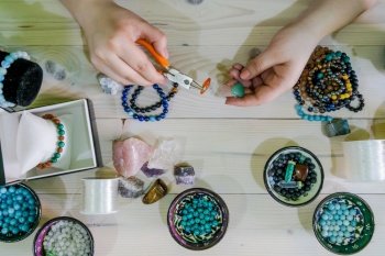 High angle view of Young woman making crystal jewelery necklace and bracelet at home manually