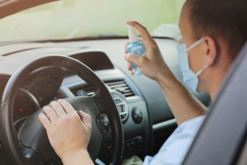 Spraying antibacterial sanitizer spray on steering wheel car, infection control concept. Prevent Coronavirus, COVID-19, flu. Disinfecting wipes. Man wearing in medical protective mask driving a car.. Spraying antibacterial sanitizer spray on steering wheel car, infection control concept. Prevent Coronavirus, COVID-19, flu. Man wearing in medical protective mask driving a car. Disinfecting wipes.