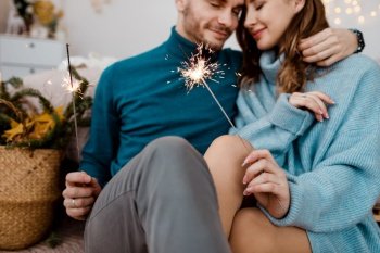 Burning sparklers in hands of party guests. Couple people are celebrating christmas and holidays happily near beautifully decorated christmas tree, christmas concept