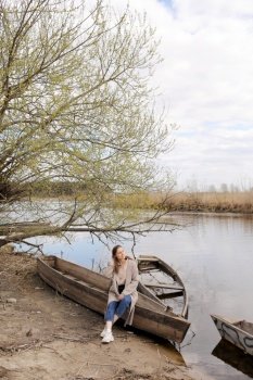 beautiful young woman is sitting and having fun in a boat near the river in spring day. beautiful young woman is sitting and having fun in a boat near the river in spring day.