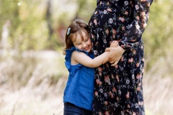 Cute little girl hugging and kissing her mother’s pregnant belly in spring nature.. Cute little girl hugging and kissing her mother’s pregnant belly in spring nature