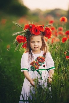 beautiful little girl with a wreath of poppies in a white dress and a bouquet of wildflowers. cute child in poppy field.. beautiful little girl with a wreath of poppies in a white dress and collects a bouquet of wildflowers. cute child in poppy field